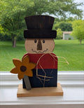 Primitive hand-painted wood scarecrow with a black top hat, stitched smile, and wooden sunflower on a wood base